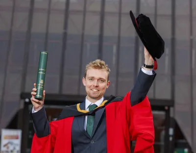 Man in red graduation robes holding a cap and scroll