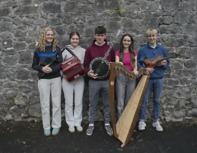 Five Irish traditional musicians standing against a wall