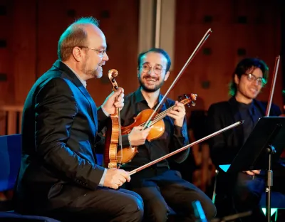 Three violinists sitting down speaking and smiling at one another