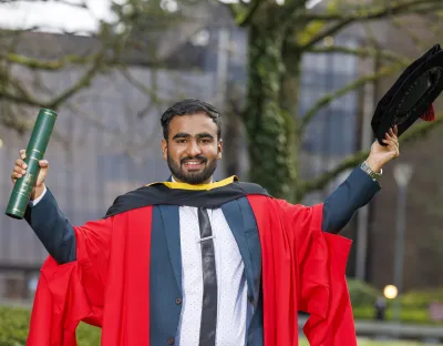 Man in PhD robes posing with hat and scroll