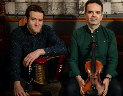 One musician holding and accordion and another musician holding a fiddle 