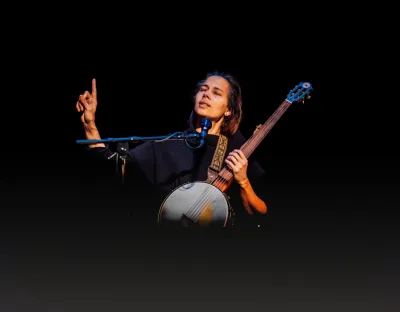 A photo of a woman playing a stringed instrument against a dark background