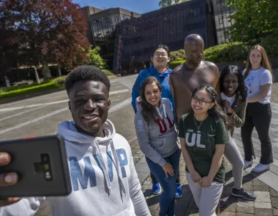 A picture of a group of students posing for a selfie beside the Brown Thomas statue on the UL campus