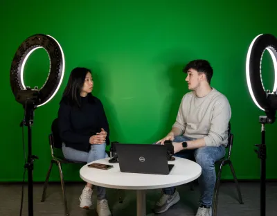 2 students in greenscreen room with laptop and ringlights