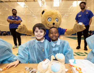 photo of two children in scrubs with giant teddy bear and two doctors behind them