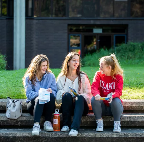 three chatting female students sitting on steps outside