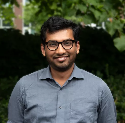 A man with black hair, beard and glasses smiling