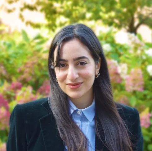 A dark haired woman wearing a black blazer and blue shirt posing