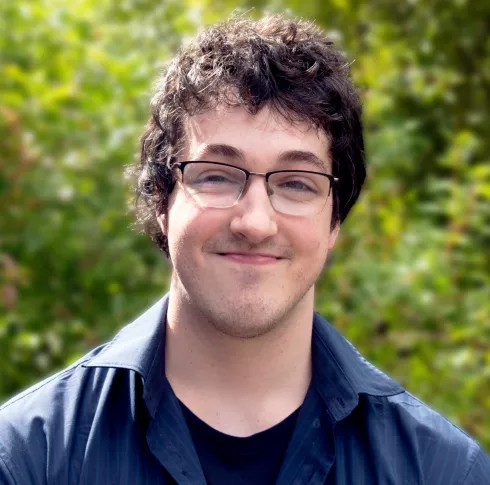 A man with dark hair ad black glasses smiling for the camera