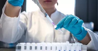 close up of gloved hands putting liquid into test tube