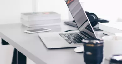 Office setting shows a desk with an open laptop beside a notebook, over ear headphones, and a phone