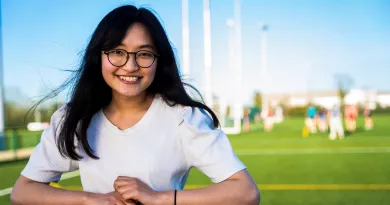 Female student leaning on railing with UL pitches in the background.