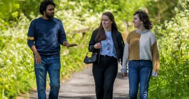 Male and two female students walking along a path, surrounded with greenery, on campus on a sunny day