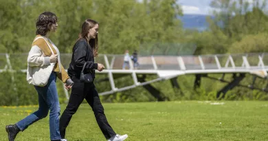 Two female students walking on a lawn with the Living Bridge in the background.