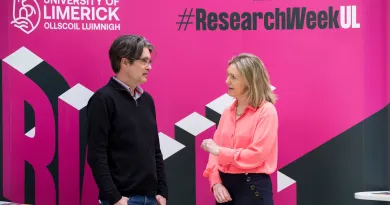 A man and a woman having a conversation in front of a Research Week banner