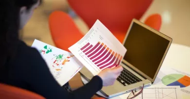 Image of person holding spreadsheet diagrams at a desk with a laptop