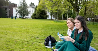 two female students sitting outside in a green area