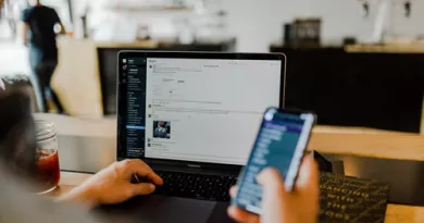 hand holding mobile phone while working on a laptop