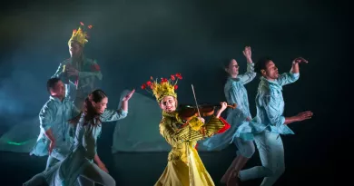 Four dancers moving across the stage with a violinist and flute player in colourful costumes