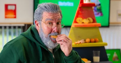 Man with a gray beard eating a cookie in front of a colorful food pyramid.