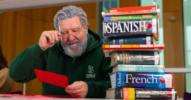 Man with a green hoodie holding a red card, next to a stack of language textbooks.