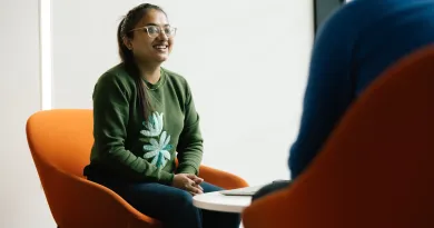 student seated on orange chair chatting with a mentor 