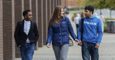 2 male postgraduate students chatting to a female student while walking