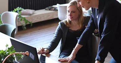 Two women looking at a laptop, one sitting down and one standing beside her