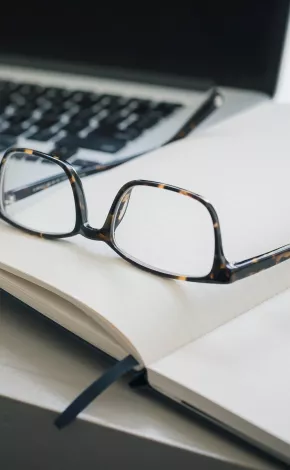 pair of glasses placed on top of an open book with a pen next to them