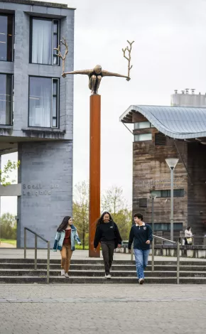 3 students chatting while walking down steps with statue in background