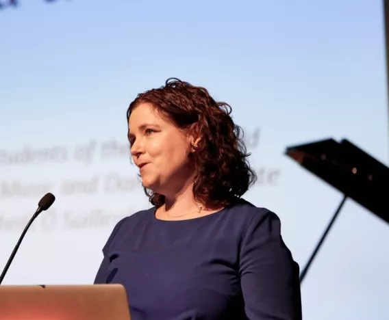 Dr. Sandra Joyce standing at a microphone delivering a talk