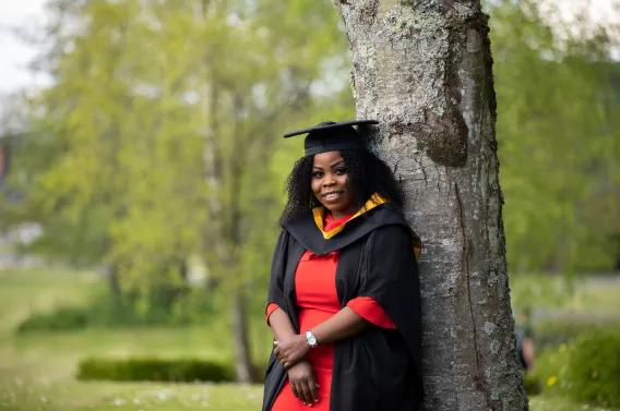 Student in graduation gown leaning against tree