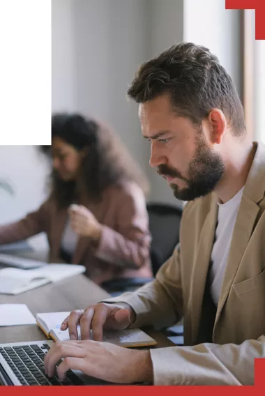 Man with beard seated at his desk on a laptop