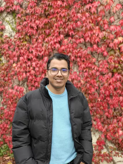 A man with glasses outside wearing a black coat and smiling