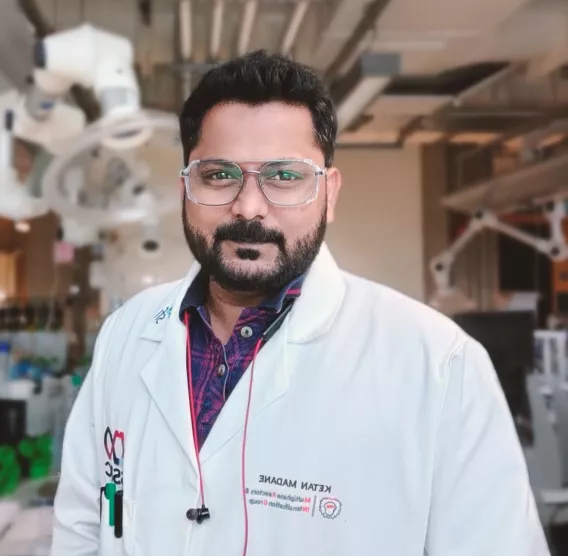 A man in a lab wearing a white coat and safety glasses