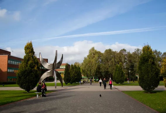 View from KBS of statue outside Schumann Building with people walking in front and trees in the background. 