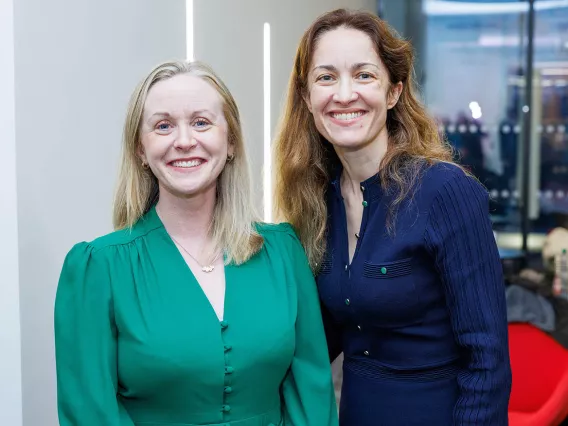 A woman in a green dress standing next to a woman in a navy dress smiling for the camera