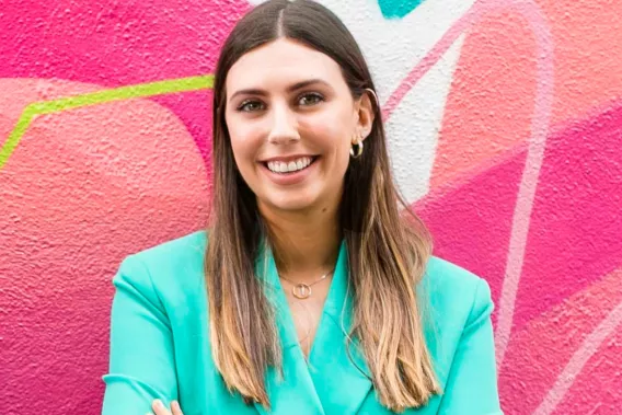 A woman in a bright green suit jacket standing against a wall with a pink mural