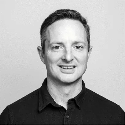 A man with dark hair, wearing a black shirt smiling