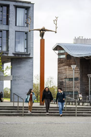 3 students chatting while walking down steps with statue in background