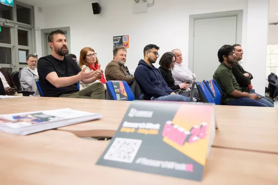 A research week banner in the foreground and a group of people in the background listening to a talk 