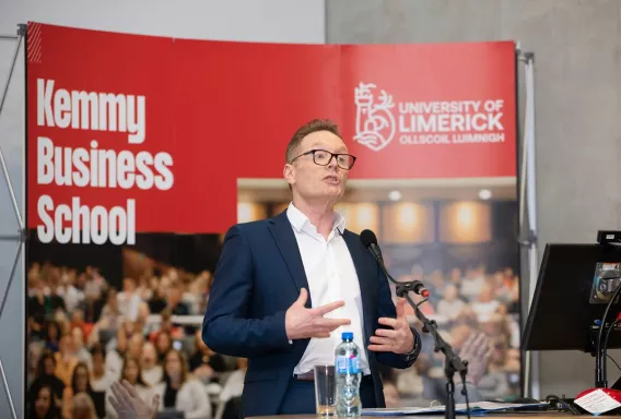 A man speaking in front of a Kemmy Business School banner