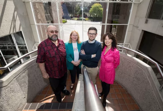 Four people standing side by side on a stairway looking towards the camera