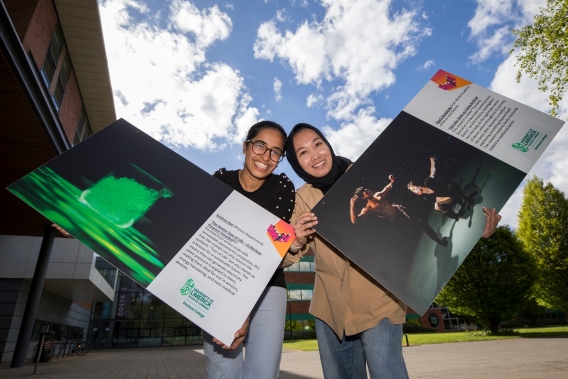Two women holding large posters showing their picture entries for a competition 