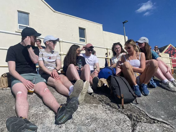 A group of seven men and women wearing summer clothes sitting on rocks with a blue sky behind them