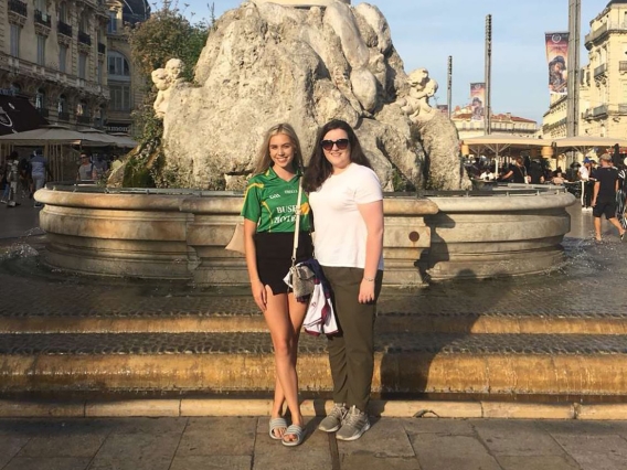 Two women standing in front of a fountain on a sunny day