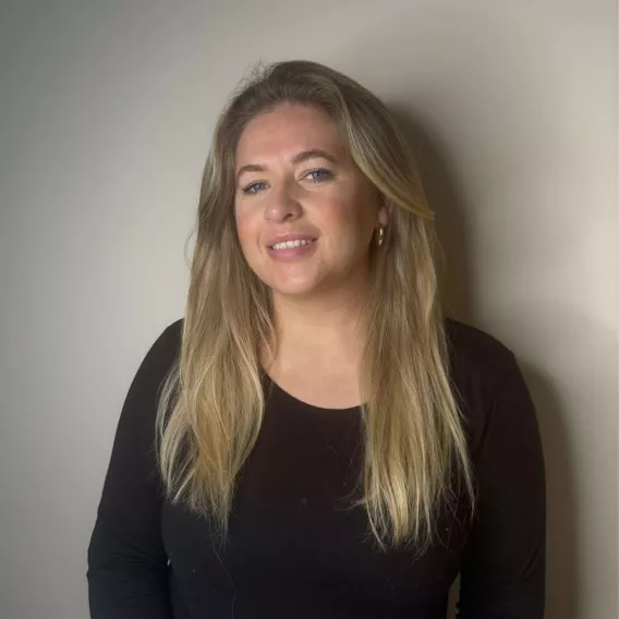 Blond haired woman in a black top standing in front of a black wall