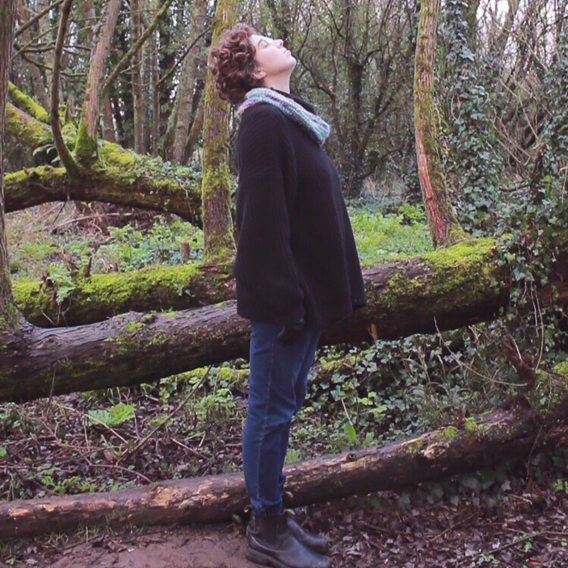 A person standing in a woodland area looking up at the sky