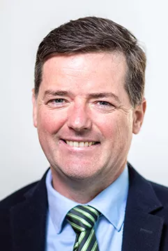 Headsot of man with short brown hair wearing a dark suit, blue shirt and stripy tie.