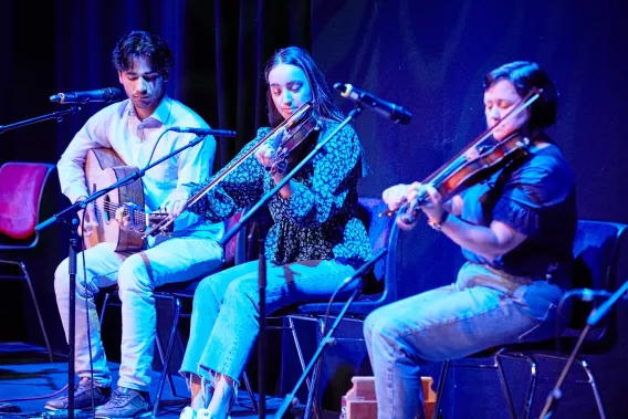 1 person playing a guitar and two people playing the fiddle